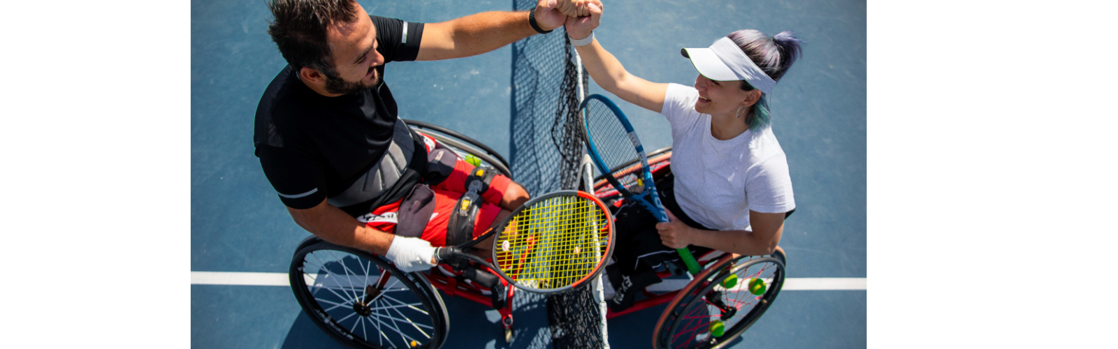 Two people in wheelchairs have tennis rackets and are shaking hands over a tennis net. 
